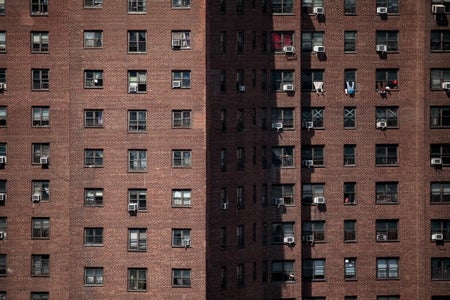 Brick building with small windows some with Air Conditioners and others with clothes hanging outside.