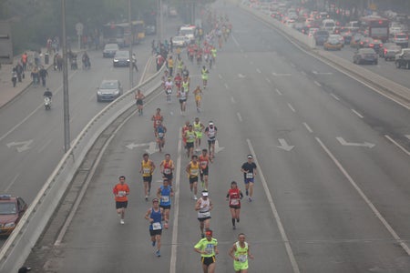 Marathon participants on a closed highway run through smoggy air