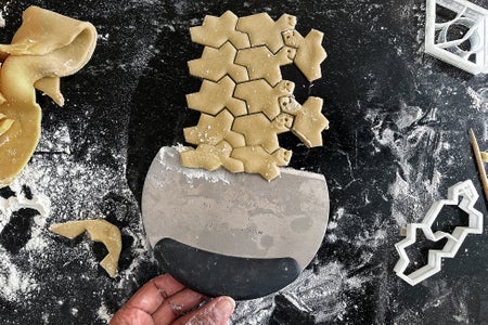 Cookie dough which has been stamped in a tessalating pattern by a 3D printed cookie cutter being scraped off a counter