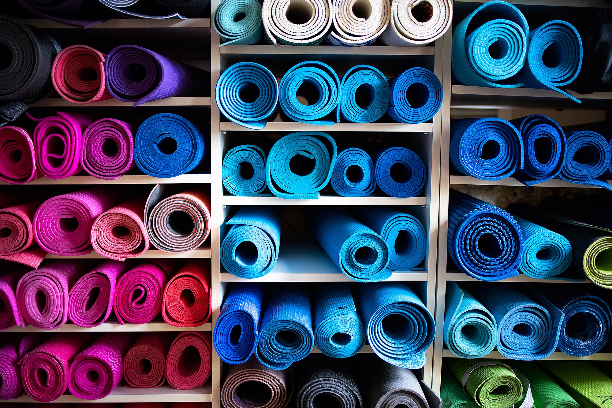 Blue and pink exercise mats lying rolled up on shelves in gym